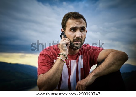 Young man talking on his cell phone. Handsome guy with beard and cell phone in nature. Outdoor picture.