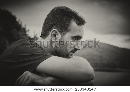 Portrait of a bearded man, wearing a red shirt and hands resting on a railing between the mountains. Black & white picture.