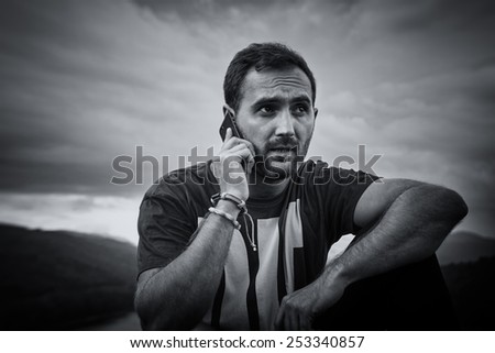 Young man talking on his cell phone. Handsome guy with beard and mobilephone in nature. Outdoor picture. Black & white picture.