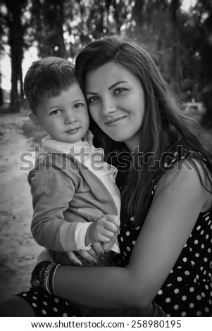 Loving young mother hugging her little son outdoors, in the park. Black & white outdoor picture.