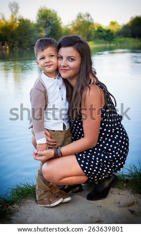 Loving young mother hugging her little son outdoors, near a lake.