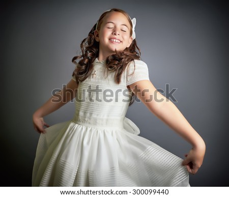 Beautiful young girl dressed in white, dreaming and dancing like a princess. First Communion. Perfect teeth and smile, long curly hair. Dark background, studio shoot.