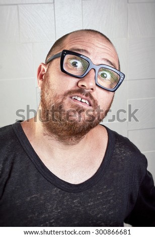 Surprised bearded guy with glasses. Unshaven guy with wide eyes and mouth open looking at the camera. Portrait over textured background.
