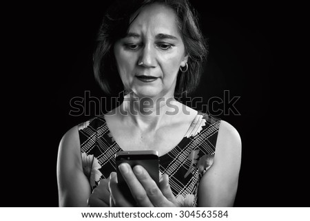 Middle aged woman writing or reading information from a mobile phone. Business woman is connecting with people. Black and white picture, black background.