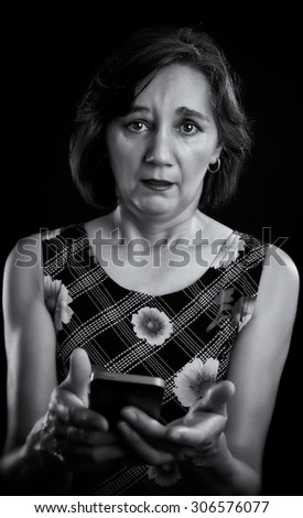 Portrait of a surprised woman, middle aged, with the mobile phone in her hands. Black & white picture over black.
