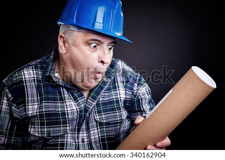 Architect with helmet looking surprised at the rolled-up plans.