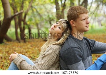 Two young people sitting back to back in autumn park