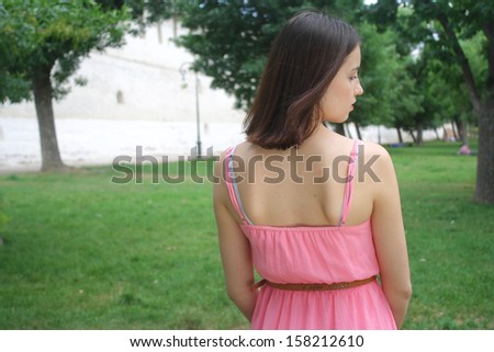 young brunette woman with pink dress standing back  in green park