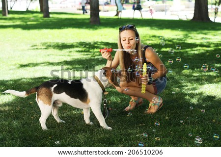 Young woman playing with dog and blowing soap bubbles outdoors in the park.
