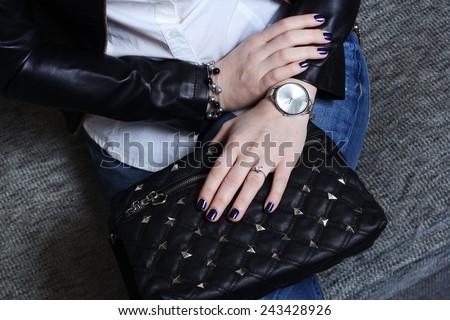 Fashionable stylish young woman in jeans and black leather jacket with black handbag and silver watch
