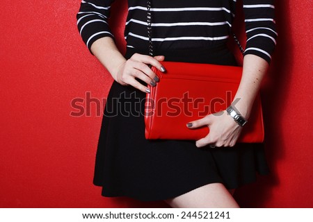 Trendy young girl in black skirt and striped shirt holding red leather handbag red background
