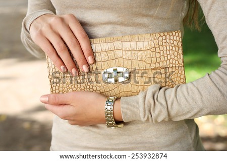 spring outdoor fashion young woman hold beige purse clutch in hand