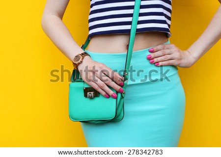 Fashionable young woman with small green handbag close up . Outdoor trendy outfit blue skirt with striped top