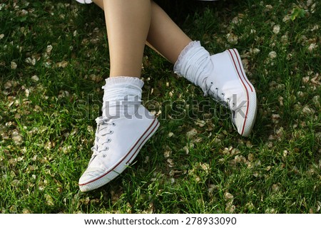 white sneakers on girl legs on grass during sunny summer day.
