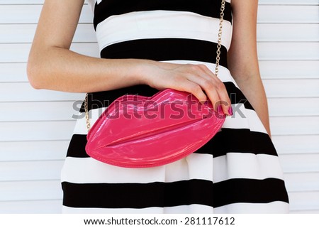 trendy girl in elegant striped dress with pink lacquered clutch in her hands. Outdoor shot