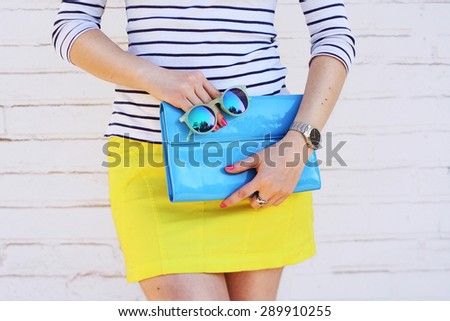 Fashion young girl hold blue clutch handbag and mirror sunglasses. Summer spring concept accessories
