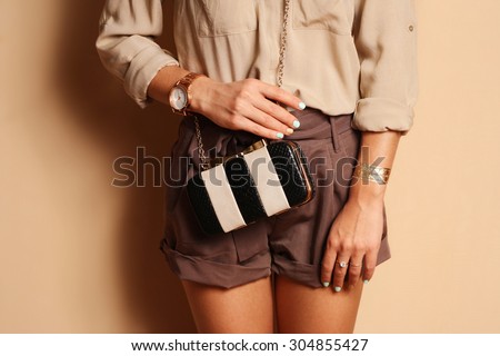 Fashionable woman with  stylish black and white clutch , accessories, watch . Elegant outfit silk blouse and  brown shorts