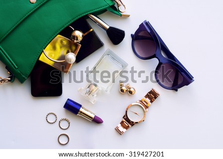 Top view of female fashion accessories for woman. Stylish sunglasses, green bag , gold watch , lipstick , perfume , rings , smart phone