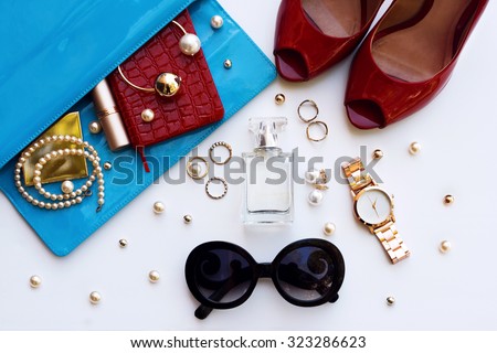 Fashionable female accessories watch sunglasses lipstick blue clutch and red shoes . Overhead of essentials for stylish young woman.