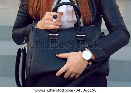 Trendy young girl in black leather jacket holding big black handbag street background .  Fashion accessories