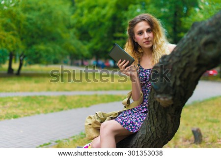 Young woman using tablet outdoor sitting on tree, weird, smile.