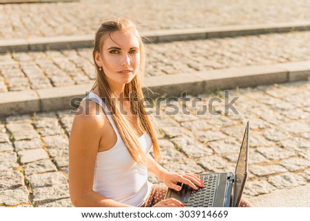 Student, in business style casual dressed, sitting in park working on laptop at campus