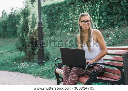 Student, in business style casual dressed, sitting in park working on laptop at campus