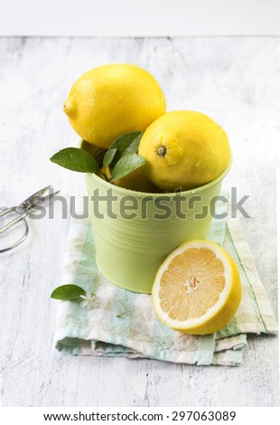 Lemon in green steel container on white wooden table top. Food styling.