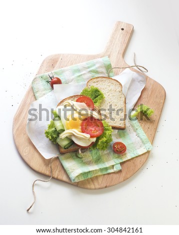 Open egg sandwich on wooden chop board with paper wrapper. White background. Table top view.
