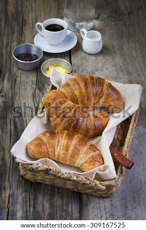 Freshly baked french croissant served with jam and butter  in food tray on rustic wooden table top. Coffee and milk in the background.
