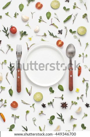 Flat lay overhead view cutlery set, plate and a blank text space invitation card on white background with vegetables, herbs and spices. Invitation or menu design background.