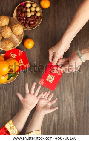 Chinese lunar new year flat lay traditional food and offering on table top. Senior women hands giving red packet to toddler boy hands.