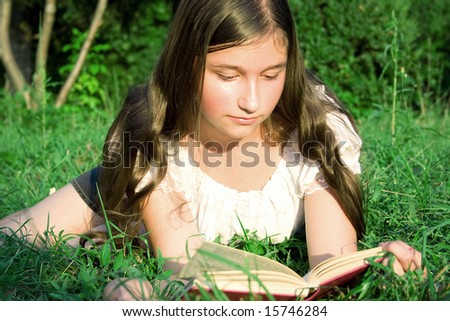 The young girl reads the book, laying on a grass
