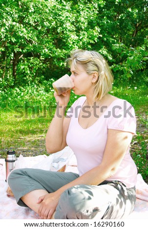 The young women on picnic drinks from a cup