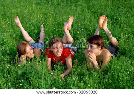 Three young beautiful girls lay in a green summer grass