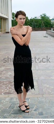 Young sad girl in black dress against urban landscape