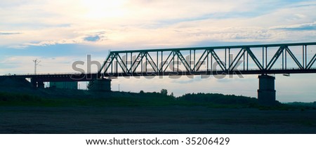 The industrial bridge through the river against the sunset evening sky