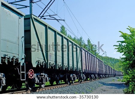 Rusty brown and green freight cars passing over a grade crossing against blue sky
