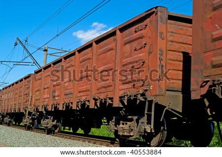 Rusty brown freight cars passing over a grade crossing against blue sky
