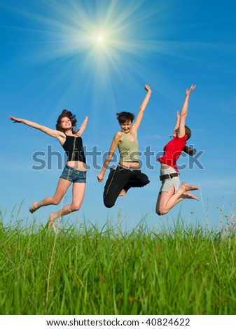 Girls jump on the meadow against blue summer sky