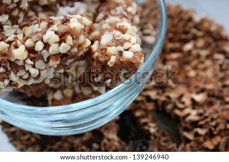 Clear glass bowl with sweet,healthy treat of dates rolled in chopped nuts on wood background.