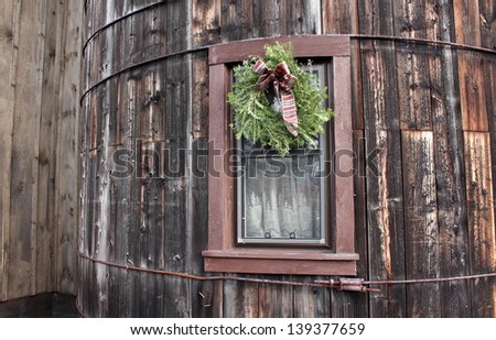 Old wood silo with holiday wreath decorated with pretty patterned bow on curtained window