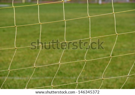 Thick yellow knotted fiber netting used to catch goals of coached soccer games on school yard field.