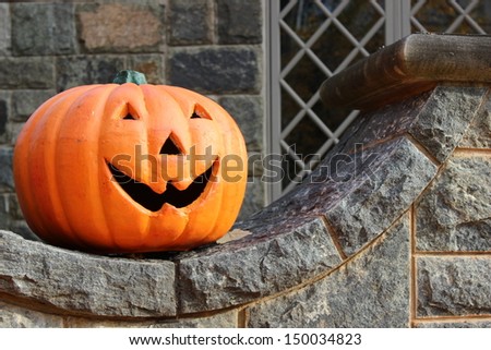 Big orange Jack-O-Lantern used as scary Halloween decoration, sitting on old curved stone wall,ready to scare those passing by .