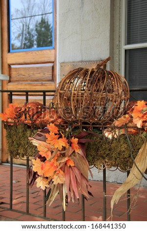 Pretty metal pumpkin and Fall\'s colorful leaves in window box outside home makes anyone visiting feel welcome.