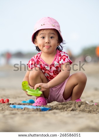 Toddler sitting alone on sandy beach doing sand play