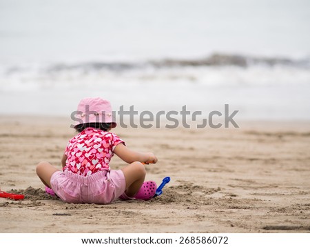 Toddler sitting alone on sandy beach doing sand play