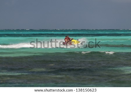 Father and daughter riding a jet ski in colorful green water, Bahamas.