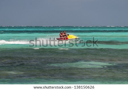 Father and daughter riding a jet ski in colorful green water, Bahamas.