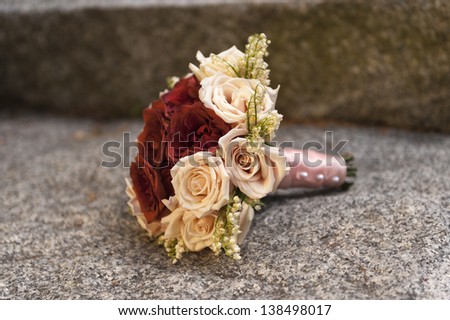 A bouquet of red and pink roses sitting on cut stone.